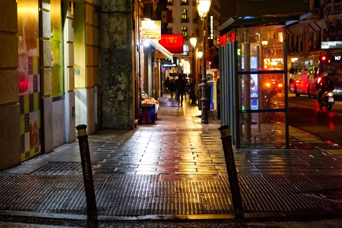 A quiet Madrid side street at night, rain-slicked and lit by shopfronts