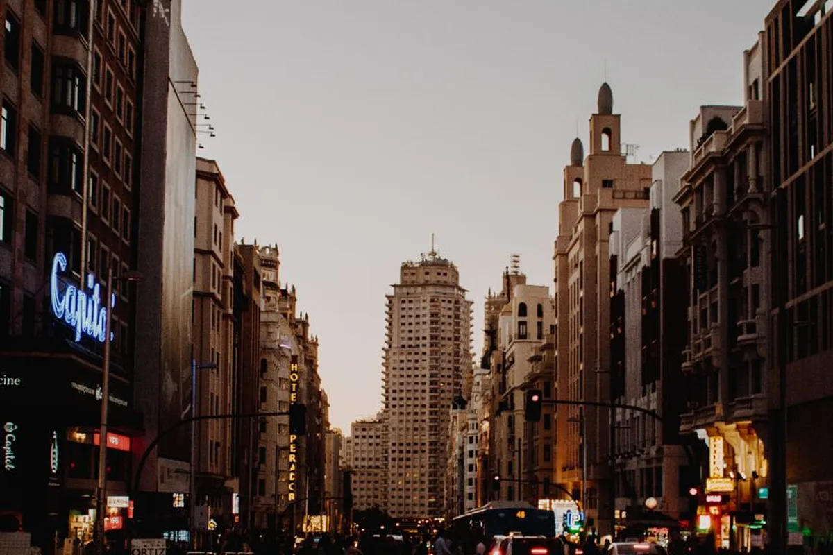 Gran Via at dusk, with the Capitol cinema's neon sign and a high-rise at the far end of the street