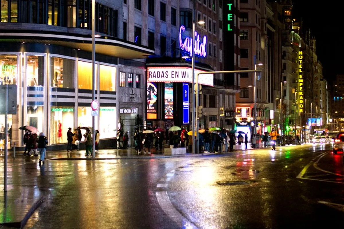 Gran Via illuminated at night in the rain, with pedestrians and neon signs