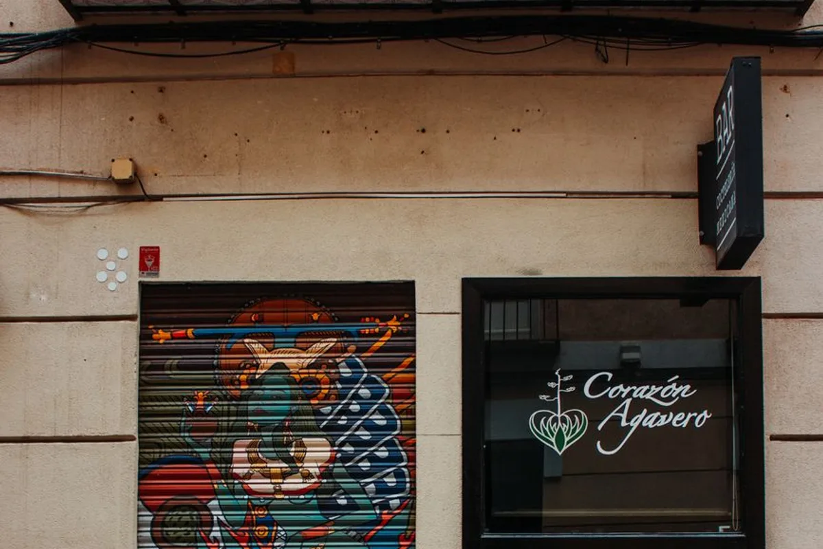 Colourful street art on a shopfront shutter beside a bar entrance in Chueca, Madrid