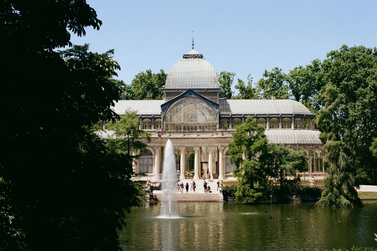 Palacio de Cristal glass pavilion reflected in a lake in Retiro Park, Madrid